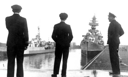 Three Royal naval officers are thinking as they observe Iroquois and the Prinz Eugen at opposite berthings in Wilhelmshaven harbour..jpg